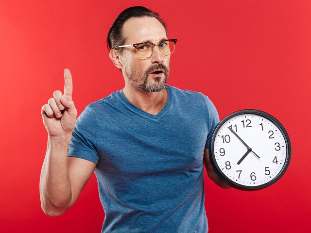 mann mit Brille, der eine Uhr hält und den Zeigefinger erhebt